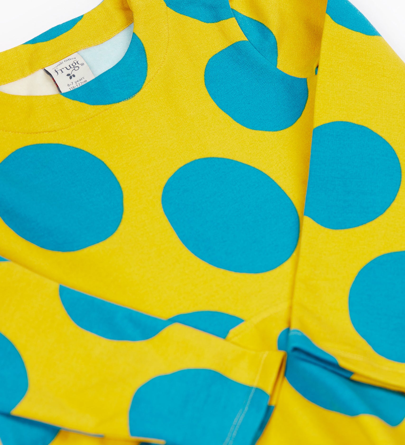 A close up of the Frugi cosy skater dress in super spot. Showing the bold blue dot print detail on yellow organic cotton fabric.