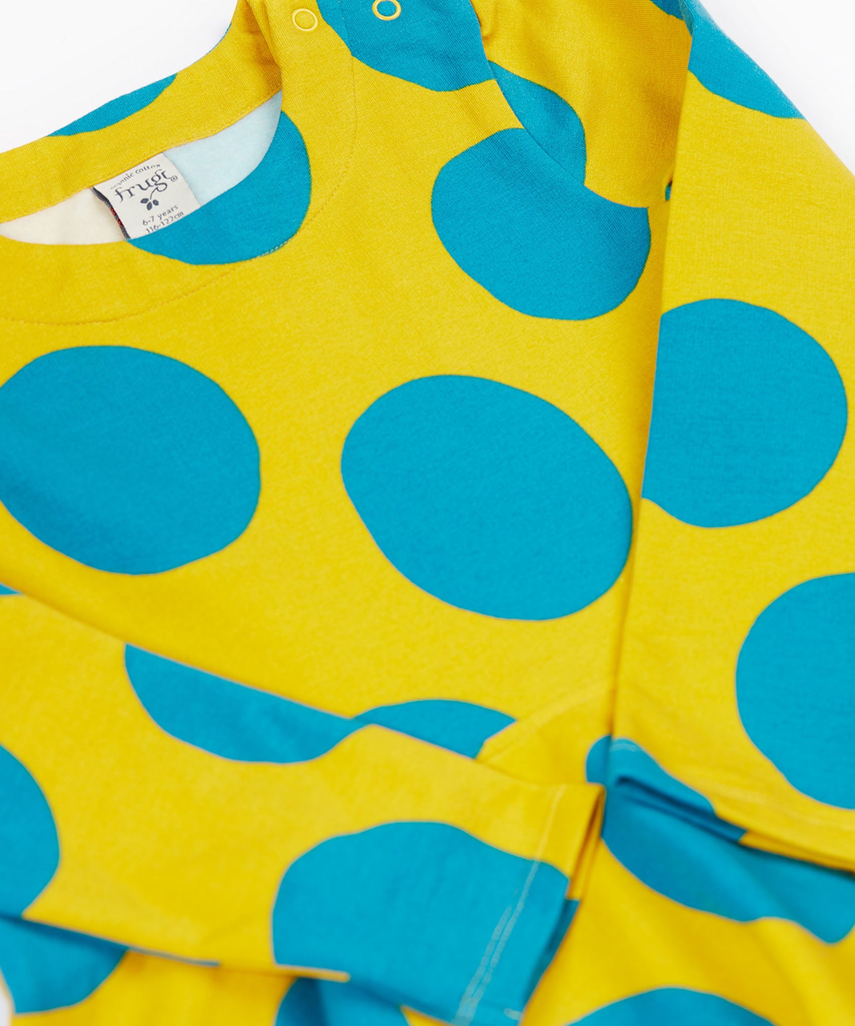A close up of the Frugi cosy skater dress in super spot. Showing the bold blue dot print detail on yellow organic cotton fabric.