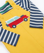 A close up of the Frugi kids coverack dungaree outfit in bumblebee/vehicle showing the red vehicle applique and button fastener detail with the striped top underneath