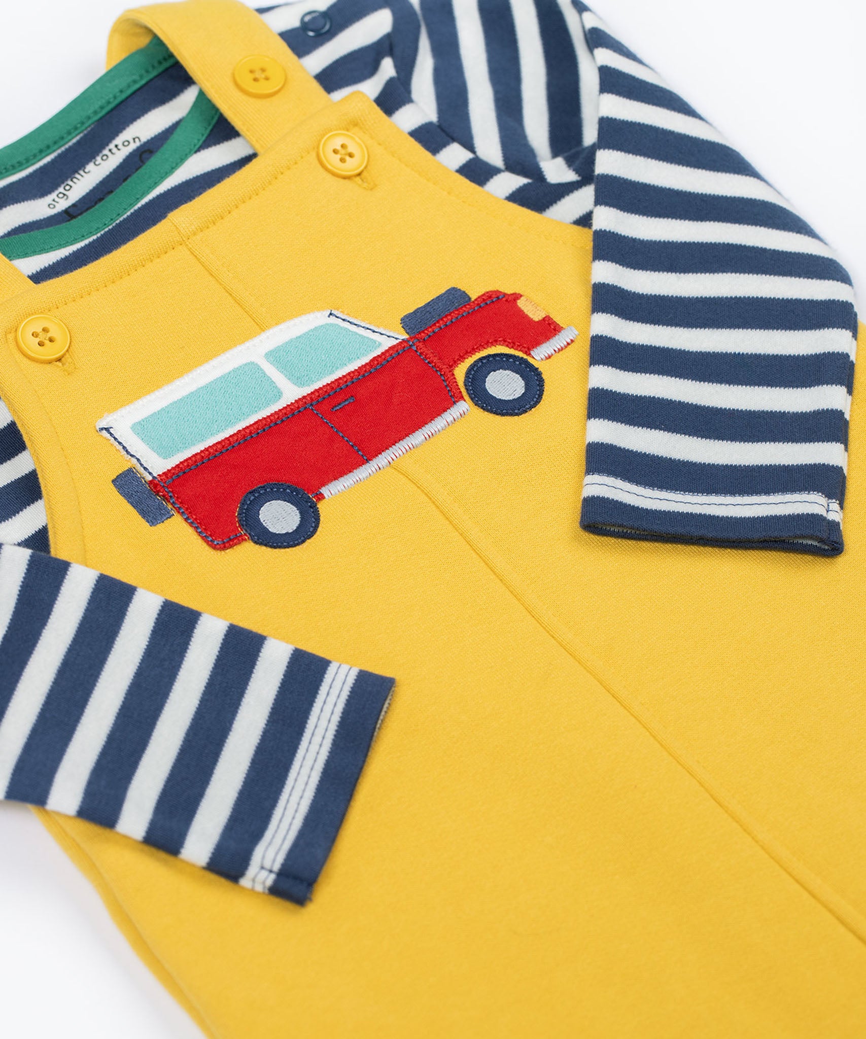 A close up of the Frugi kids coverack dungaree outfit in bumblebee/vehicle showing the red vehicle applique and button fastener detail with the striped top underneath