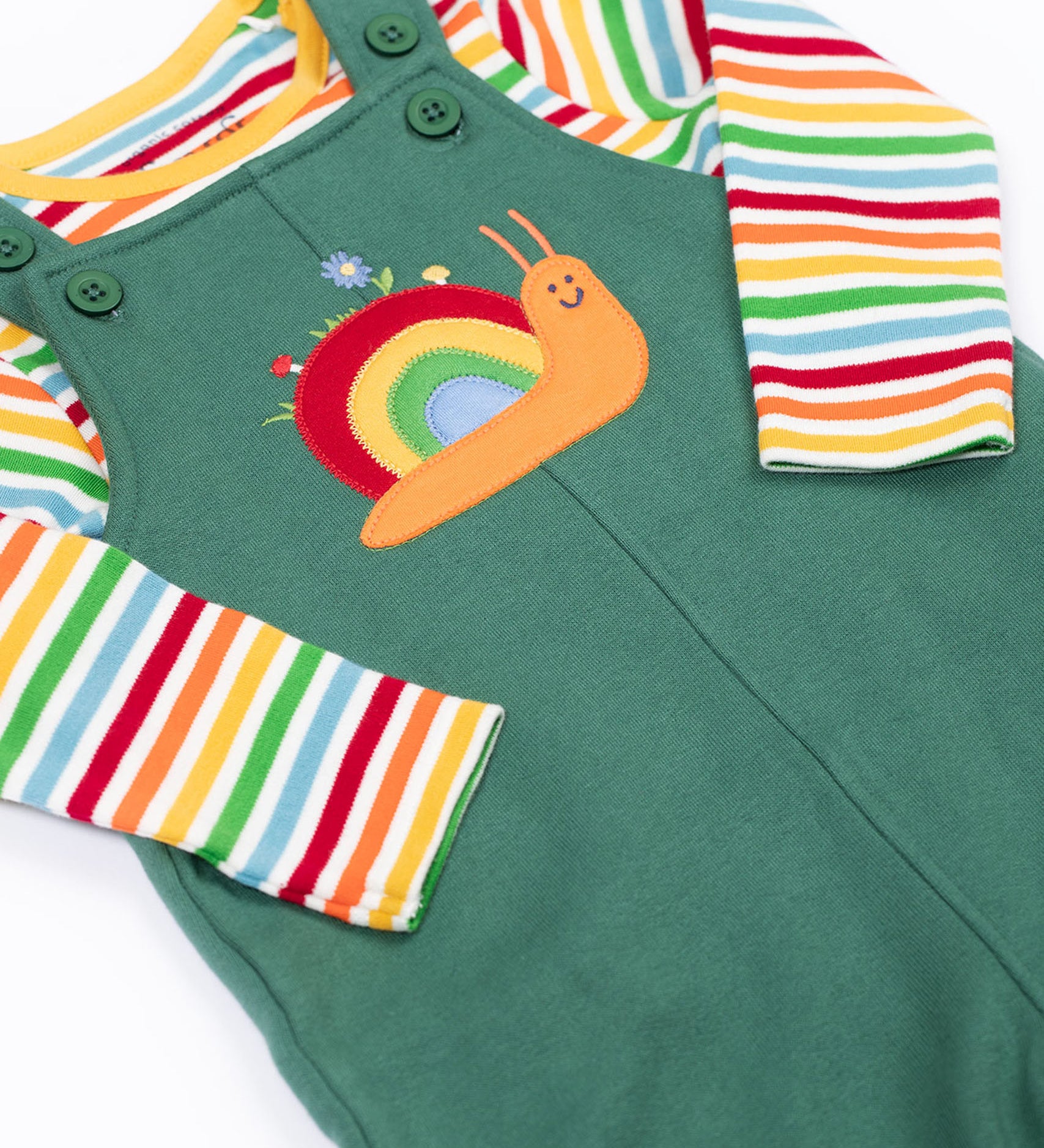 A close up of the Frugi kids coverack dungaree outfit in holly green/snail showing the playful snail applique and button fastener detail with the striped top underneath