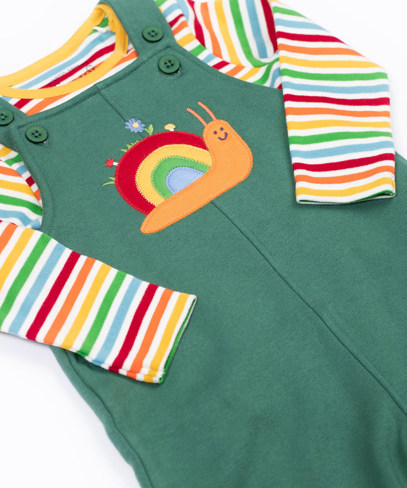 A close up of the Frugi kids coverack dungaree outfit in holly green/snail showing the playful snail applique and button fastener detail with the striped top underneath