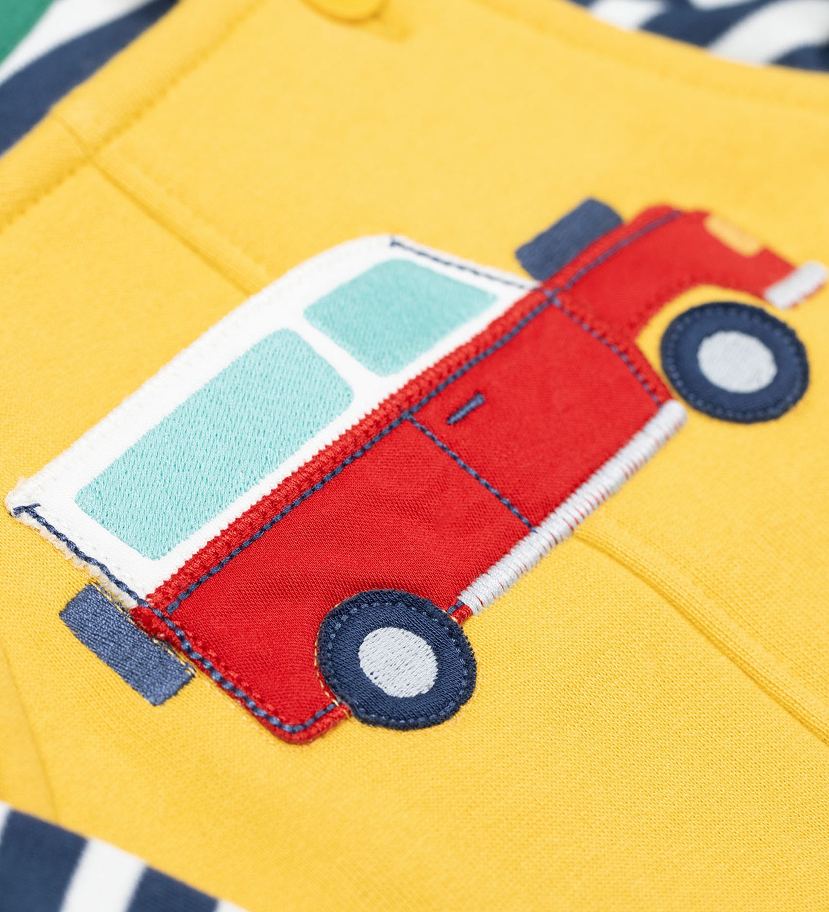 A close up of the Frugi kids coverack dungaree outfit in bumblebee/vehicle showing the red vehicle applique detail on yellow organic cotton fabric.
