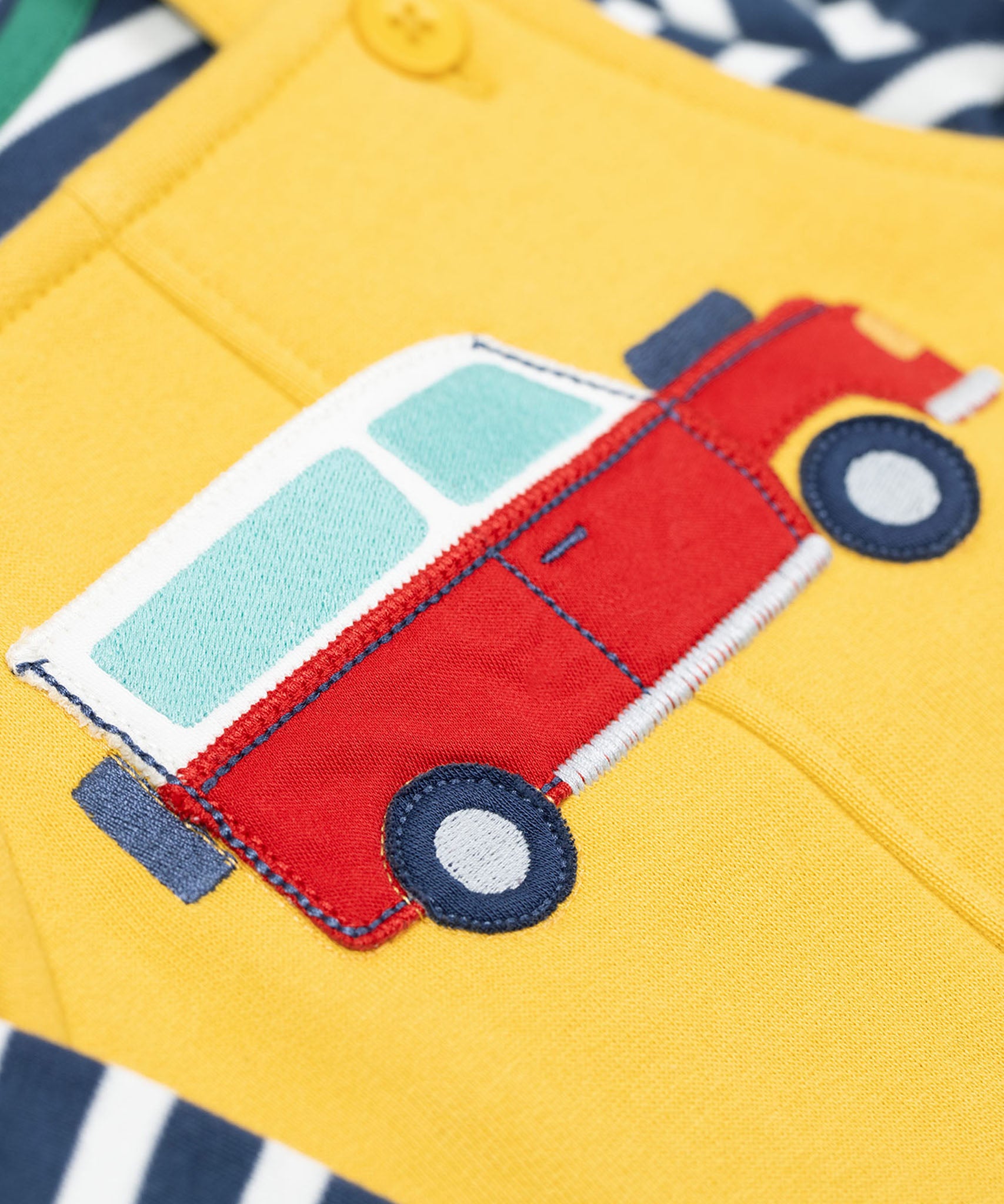 A close up of the Frugi kids coverack dungaree outfit in bumblebee/vehicle showing the red vehicle applique detail on yellow organic cotton fabric.