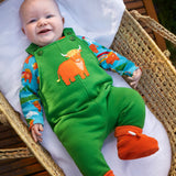 Baby wearing the Frugi coverack palm green dungaree with highland coos applique with a highland cows design long sleeve body underneath. 