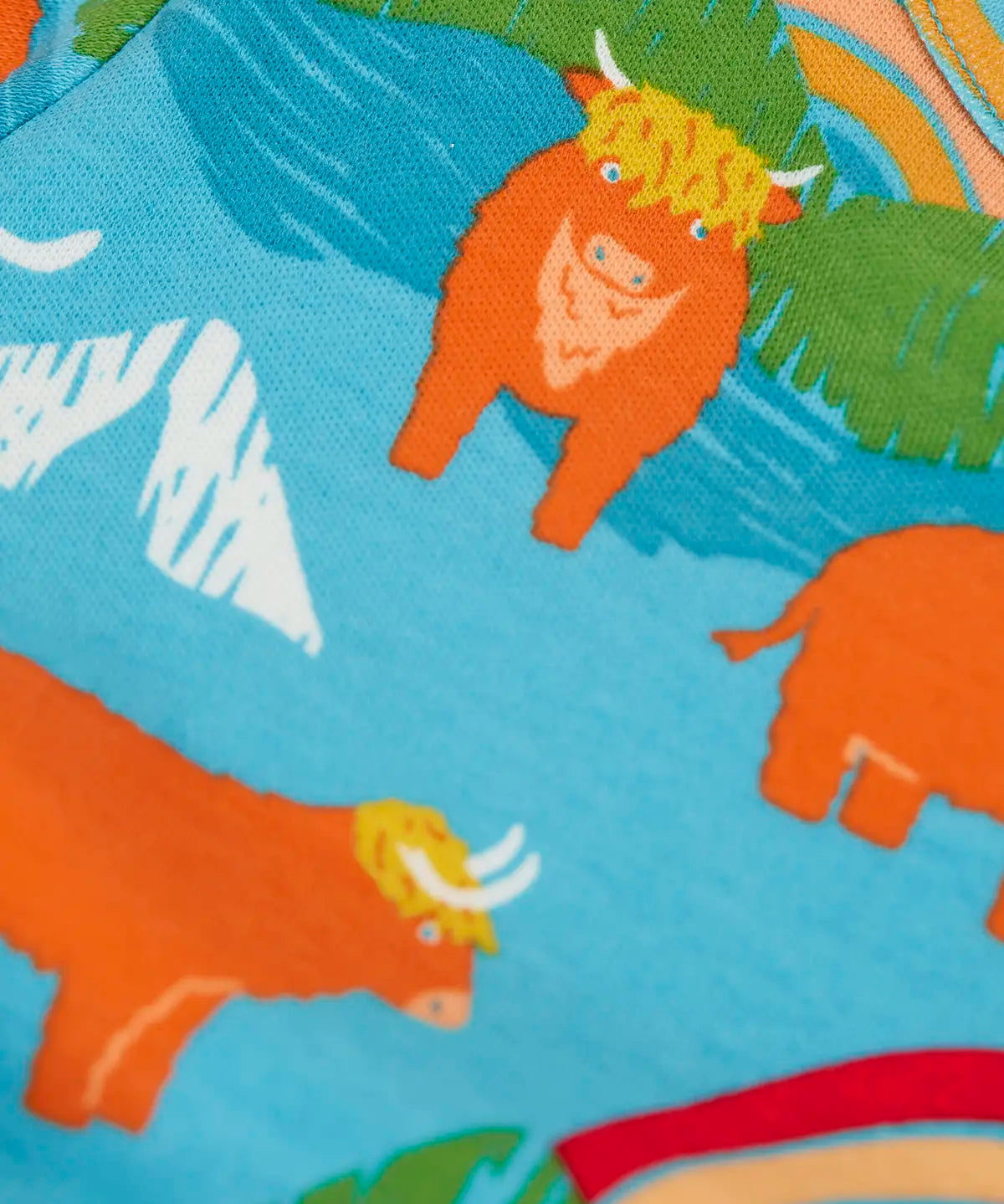 Frugi kids dungaree outfit showing a close up of the repeating highland cow print on the light blue organic cotton top 
