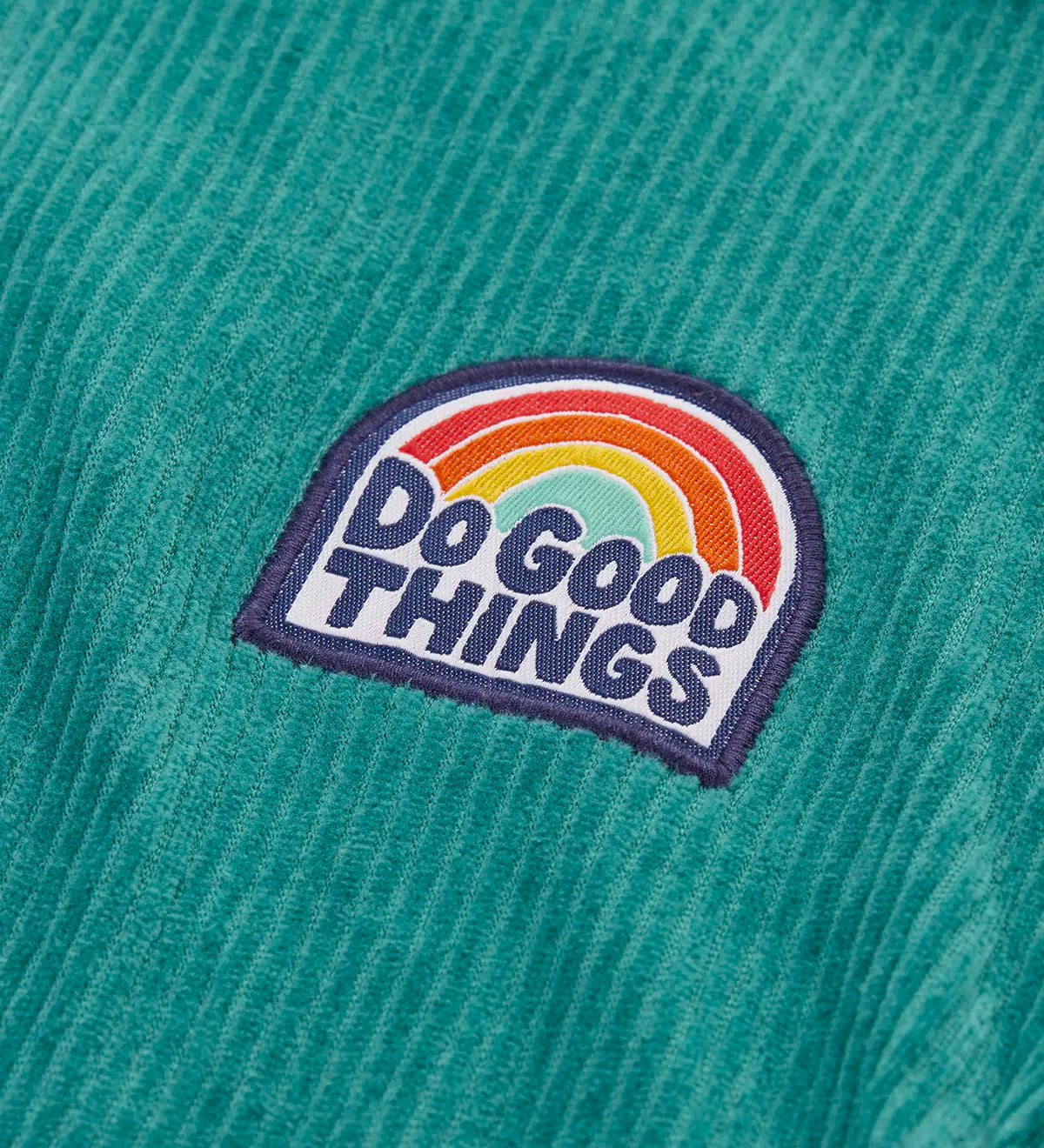 Close up of the do good things rainbow badge on the chest of the Frugi Croft organic cord half zip jumper in hut green.
