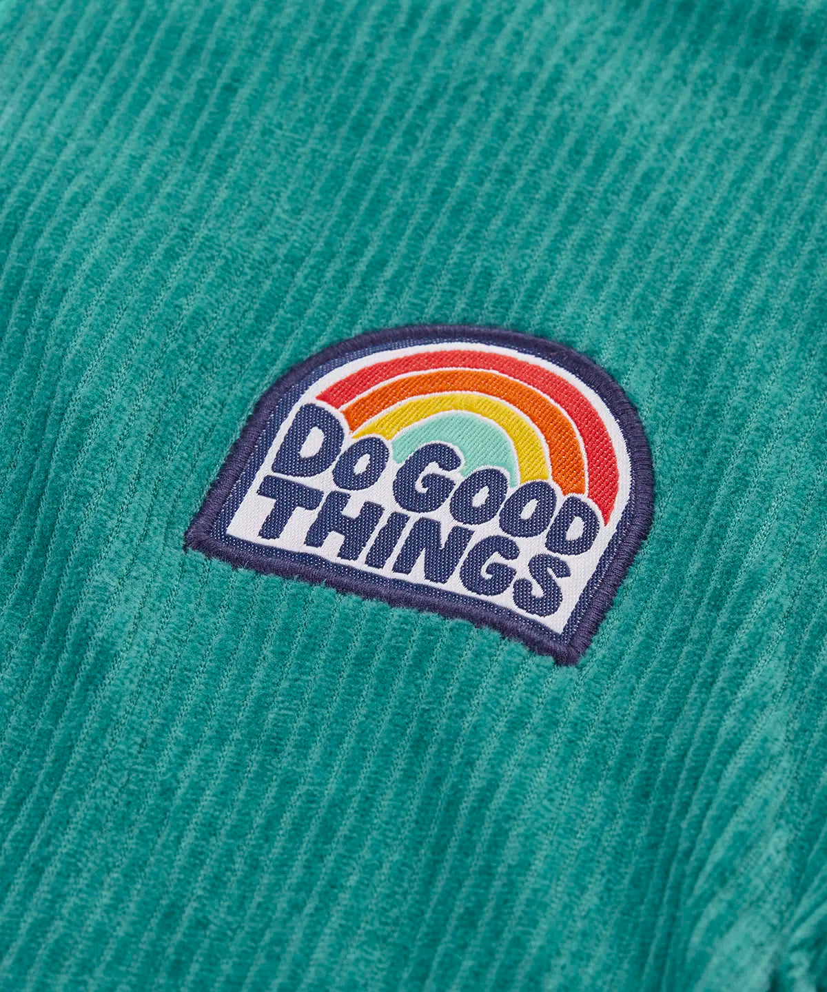 Close up of the do good things rainbow badge on the chest of the Frugi Croft organic cord half zip jumper in hut green.