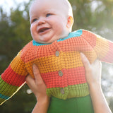 Baby wearing the Frugi cuddly knit highland wide stripe rainbow cardigan being held up. 