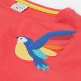 A close up of Frugi Daisy Applique T-Shirt in Watermelon's embroidered colourful parrot.