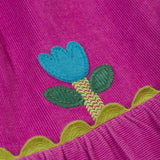 A close up of the Frugi kids holly dress in damson flowers showing the cute flower applique detail on bright purple organic cotton fabric.