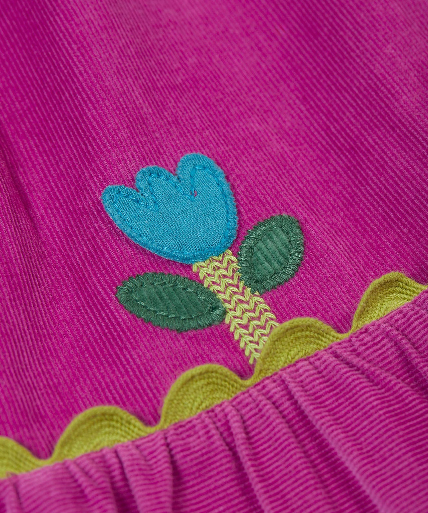 A close up of the Frugi kids holly dress in damson flowers showing the cute flower applique detail on bright purple organic cotton fabric.