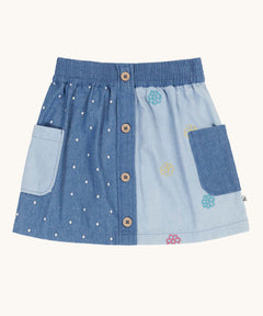 Frugi denim children's organic denim skirt with side pockets and wooden buttons down the front. One side is a darker denim with white polka dots all over with the other side being a lighter denim decorated with embroidered flower outlines.
