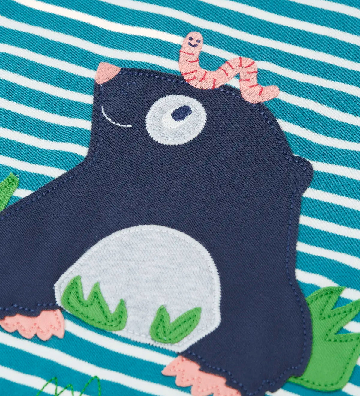 Close up of the mole applique with a worm on it's head on the front of the Frugi discovery long sleeve top in a boat blue Breton stripe.