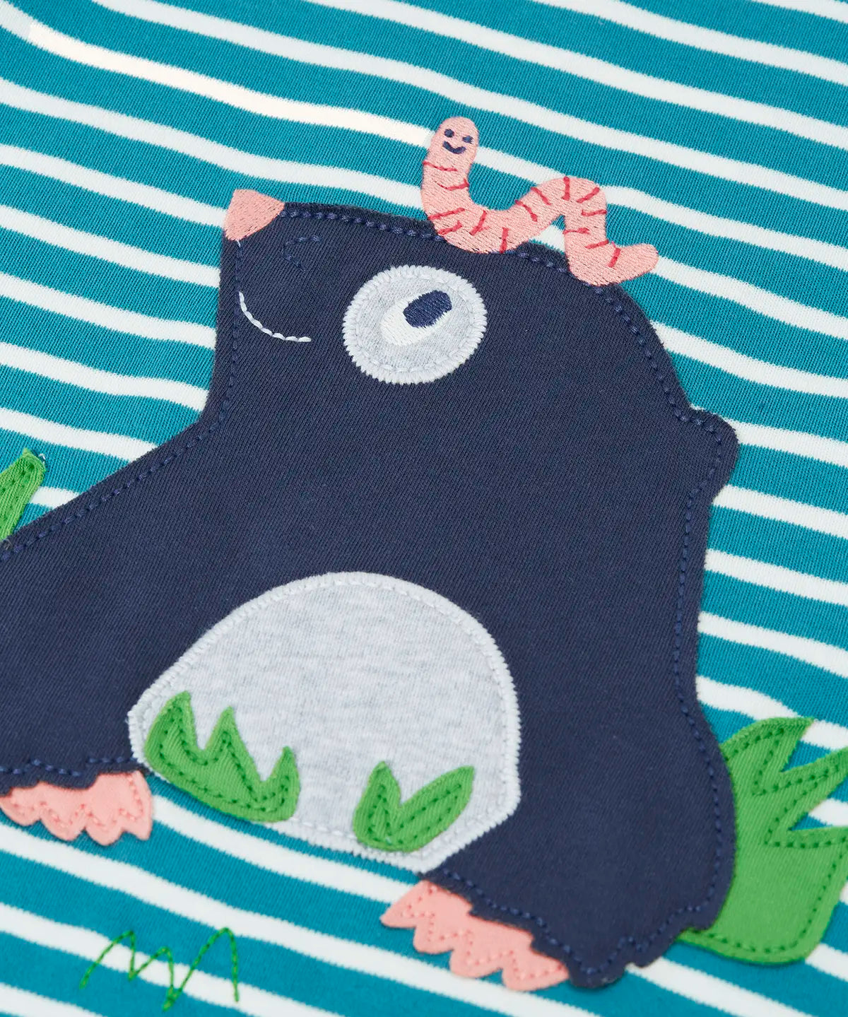 Close up of the mole applique with a worm on it's head on the front of the Frugi discovery long sleeve top in a boat blue Breton stripe.