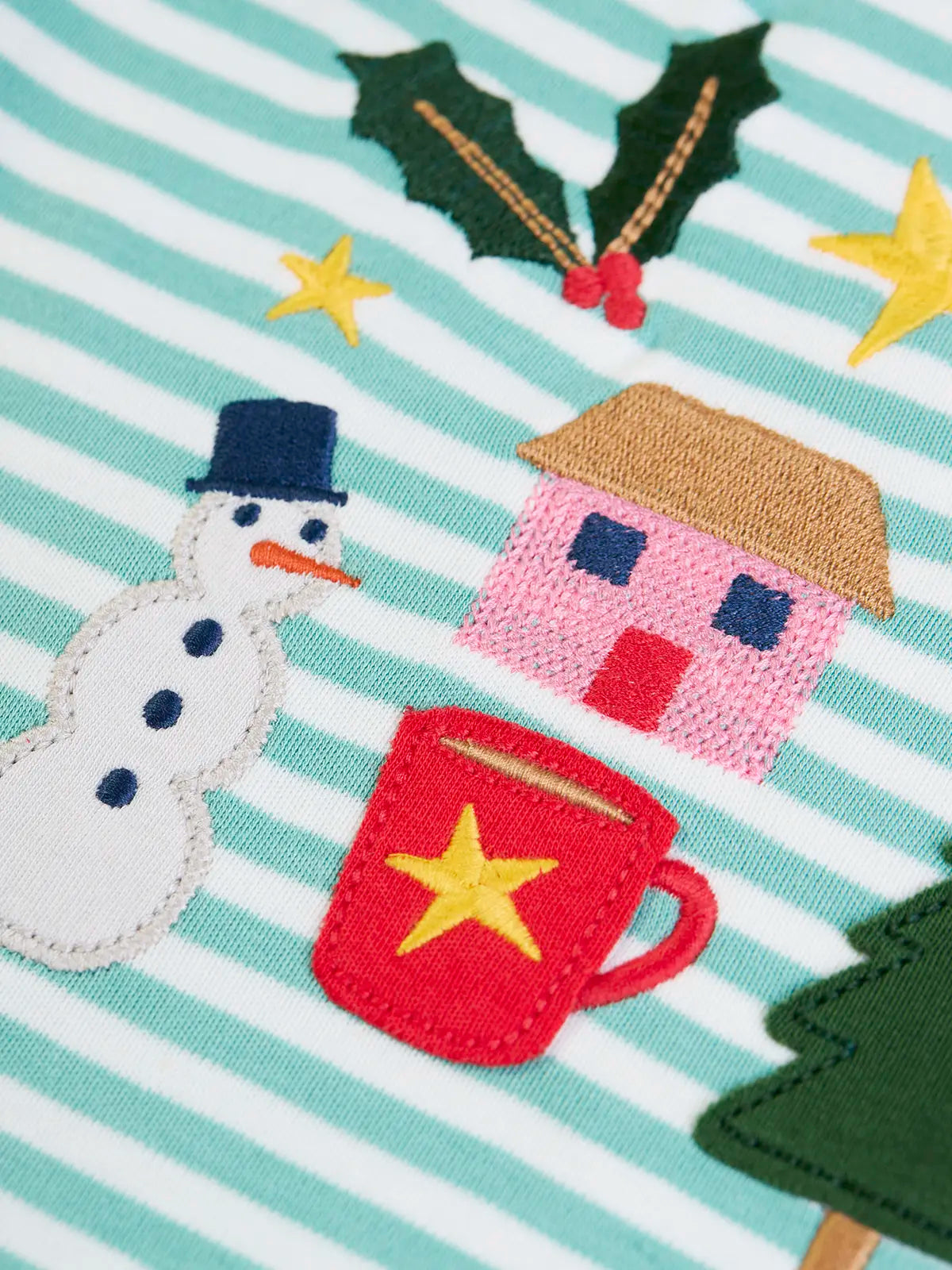 Close up of the snowman, holly tree house and hot chocolate appliques and embroidery details on the Frugi discovery organic cotton long sleeved top in miss green stripe with winter appliques.