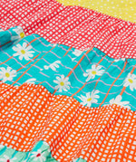 A close up of Frugi Dorothy Twirly Dress, with a Rainbow Hotchpotch print, a patchwork type design featuring orange, mint, red, yellow and green patterns with daisies.