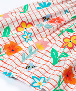 Close up of the Frugi kids Delpi paint a floral dress. Showing the gentle gather with different coloured flowers and yellow bees on white check with red outline organic cotton fabric