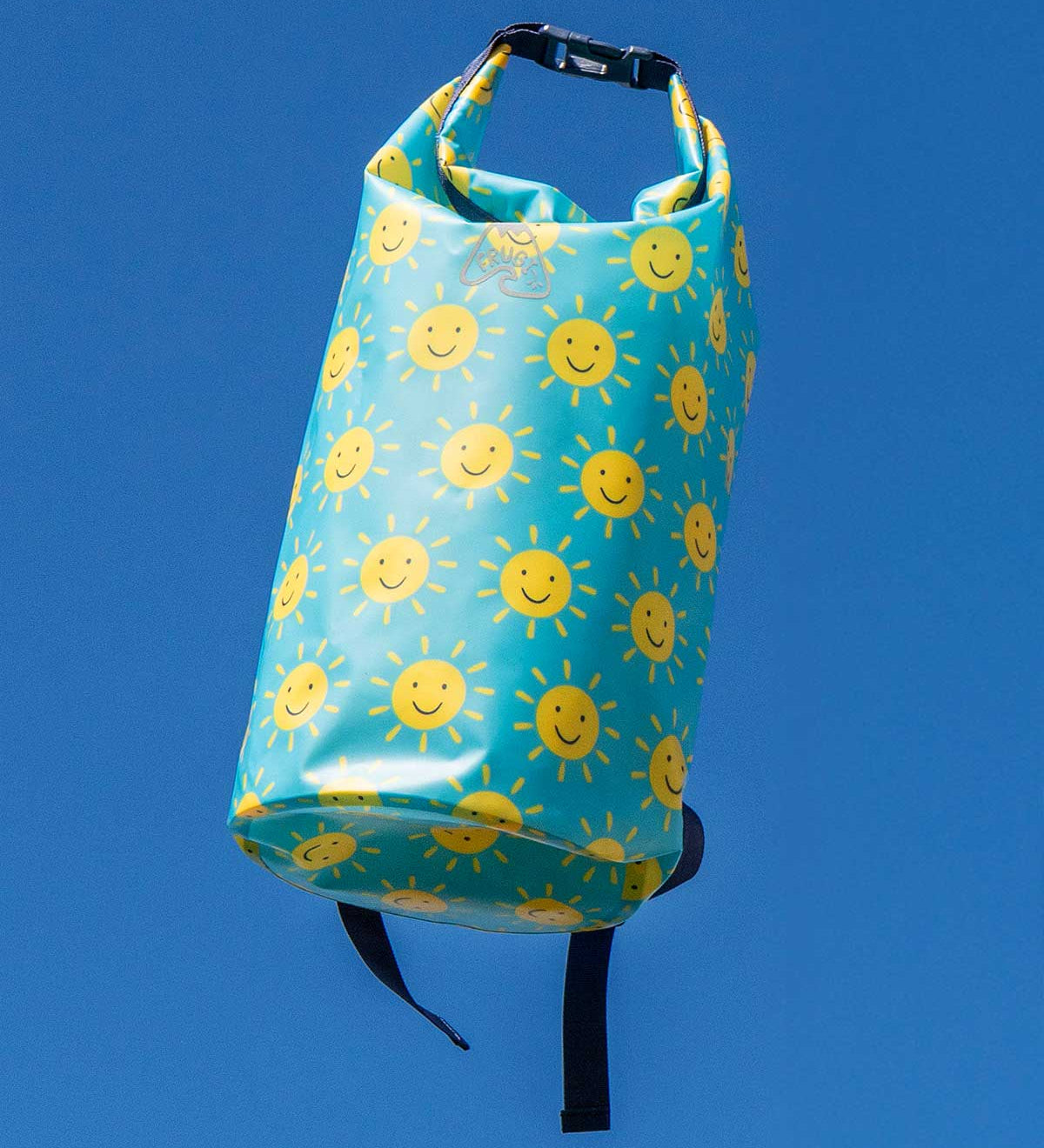 Frugi dry bag backpack, blue bag with an all over smiley sunshine print shown against a blue sky background.