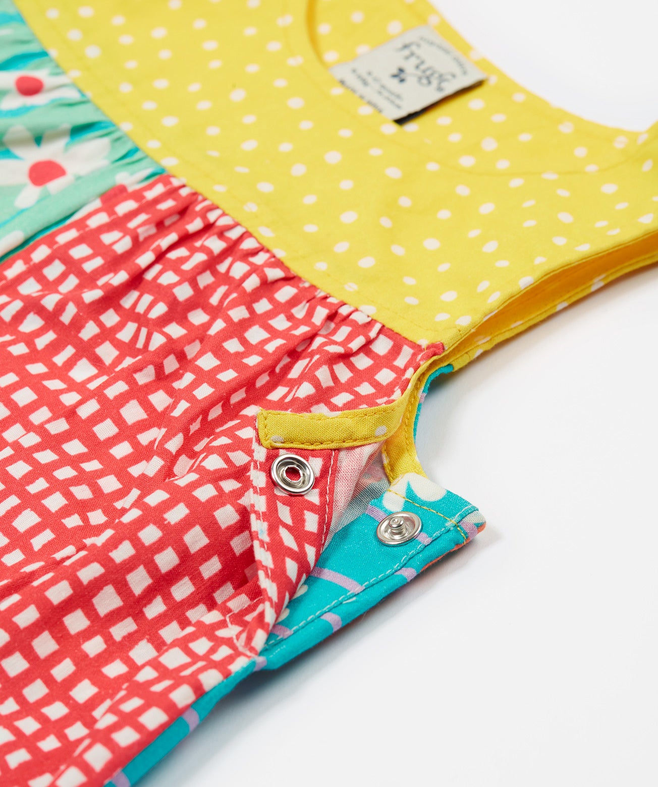 A close up of the popper fastenings on the Frugi Summer Printed Dungaree in the Rainbow Hotchpotch print.