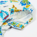 A close-up of the Frugi Aloha Organic Cotton Dungarees popper fastenings, featuring a colourful tropical beach print with dolphins, rainbows and sailing boats.