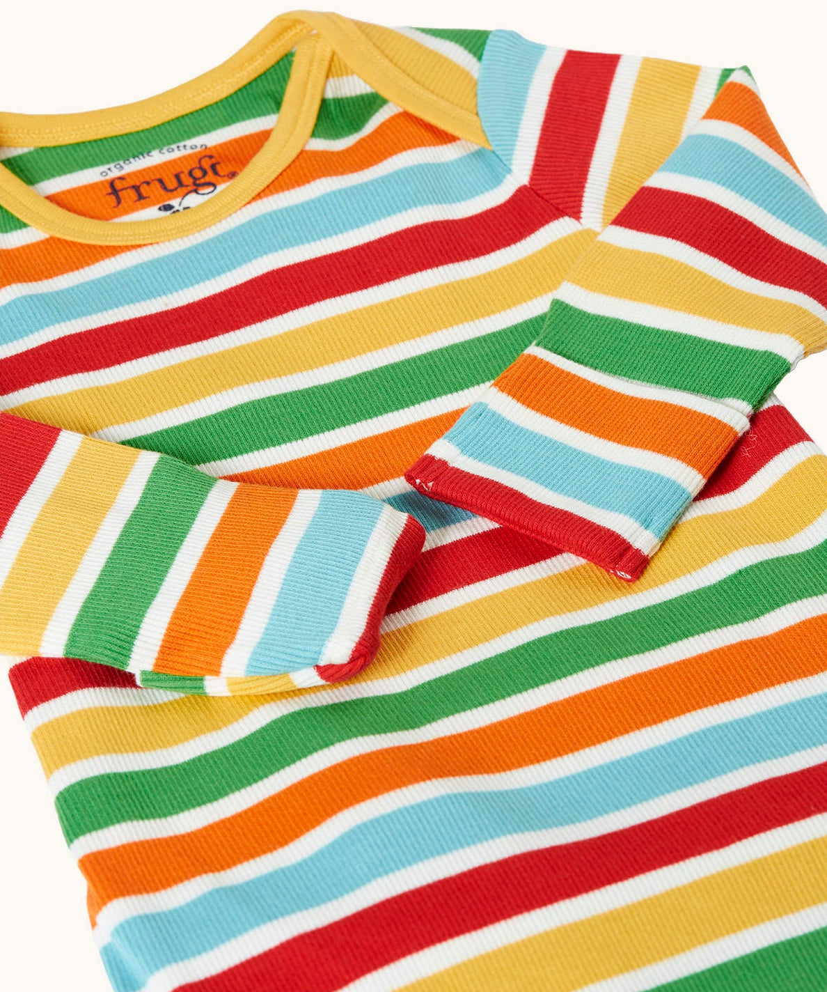 A close view of the front of the Frugi easy dressing rainbow striped ribbed material babygrow. easy access on the back to roll off the legs off for easy nappy changes. 