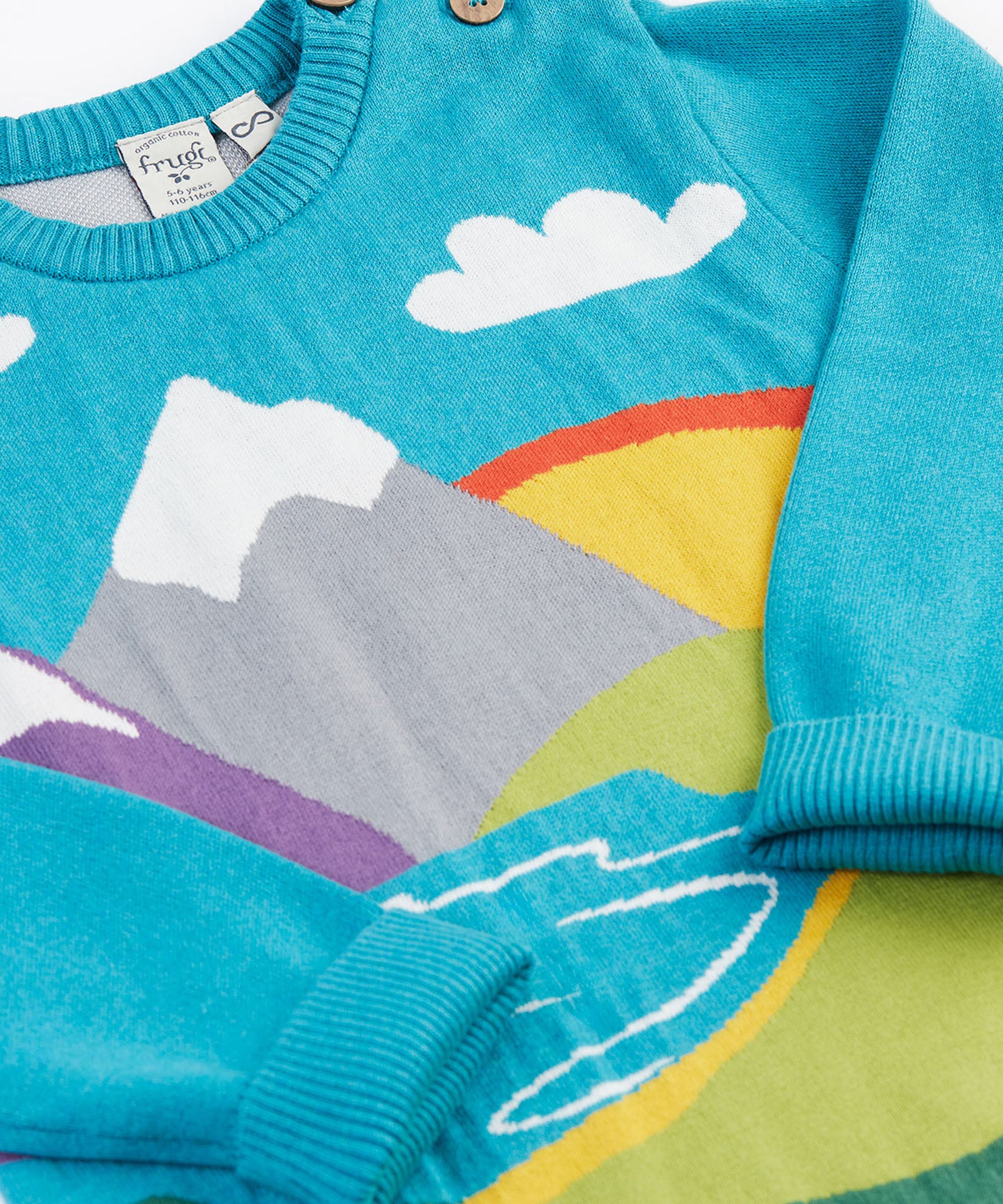 A close up of the front of the Frugi Elwood organic cotton knitted jumper with a blue mountain scene design.