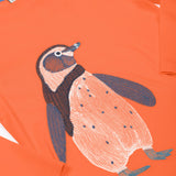 A close up of the Frugi kids embroidered adventure top in salamander/penguin showing the full penguin embroidery detail on pastel orange organic cotton fabric.