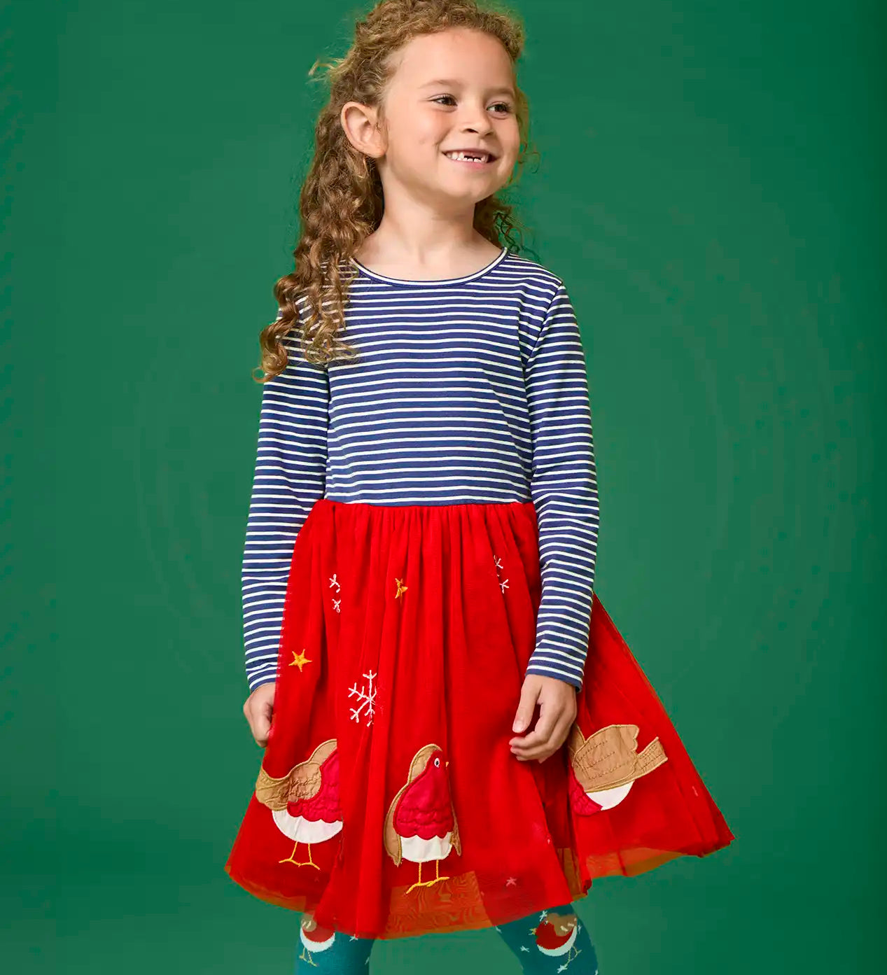 Child wearing the Frugi emmie skater dress with a long sleeved navy stripe top half and red robin applique tulle  skirt.