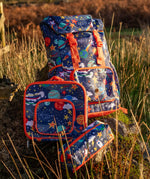 Frugi trail blazing backpack, lunch bag and pencil case in the explore the stars design standing on a rock in a grassy field