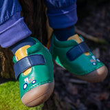 A close up of the Fjord First Walker leather baby shoes with a holly green tractor design being worn. The child is sitting outdoors.