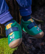 A close up of the Fjord First Walker leather baby shoes with a holly green tractor design being worn. The child is sitting outdoors.