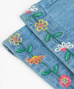 Close up of the embroidered flowers on the cuffs of the Frugi flared organic denim dungaree.