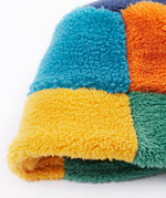 A close up of the Frugi kids fleece bucket hat in hotchpotch showing the multicoloured block detail on 100% recycled polyester fabric.