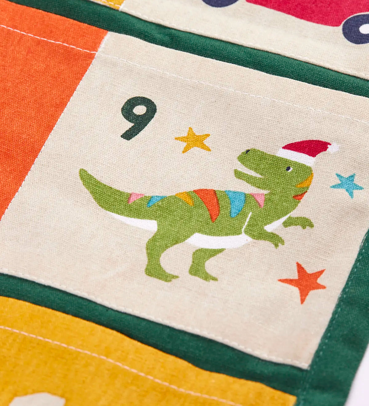 Close up of day 9 pocket featuring a t-rex dinosaur wearing a santa hat on the  Frugi forest festive fun organic cotton advent calendar. 
