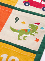 Close up of day 9 pocket featuring a t-rex dinosaur wearing a santa hat on the  Frugi forest festive fun organic cotton advent calendar. 