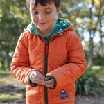 A child wearing the Frugi toasty trail reversible jacket showing the orange colour side and green zip detail with a brand patch on the side pocket on post consumer recycled polyester fabric