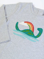 Close up of the loch ness monster applique on the front of the Frugi frankie organic cotton baby and toddler outfit with Nessie design. Long sleeved grey marl top with wide orange stripe trousers. 