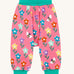 Frugi fun flowers print parsnip pants children's organic cotton trousers. The fun flowers print features multi-coloured flowers and bees on a pink background with turquoise coloured waistband and leg cuffs. 