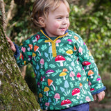 A child standing next to a tree wearing the Frugi Fun-Guys Children's Snuggle Fleece.