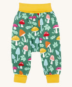 The Frugi fun guys multi coloured mushroom print parsnip pants children's trousers. The print features multi-coloured mushrooms, light green leaves on a dark green background with yellow cold coloured waistband and leg cuffs. 