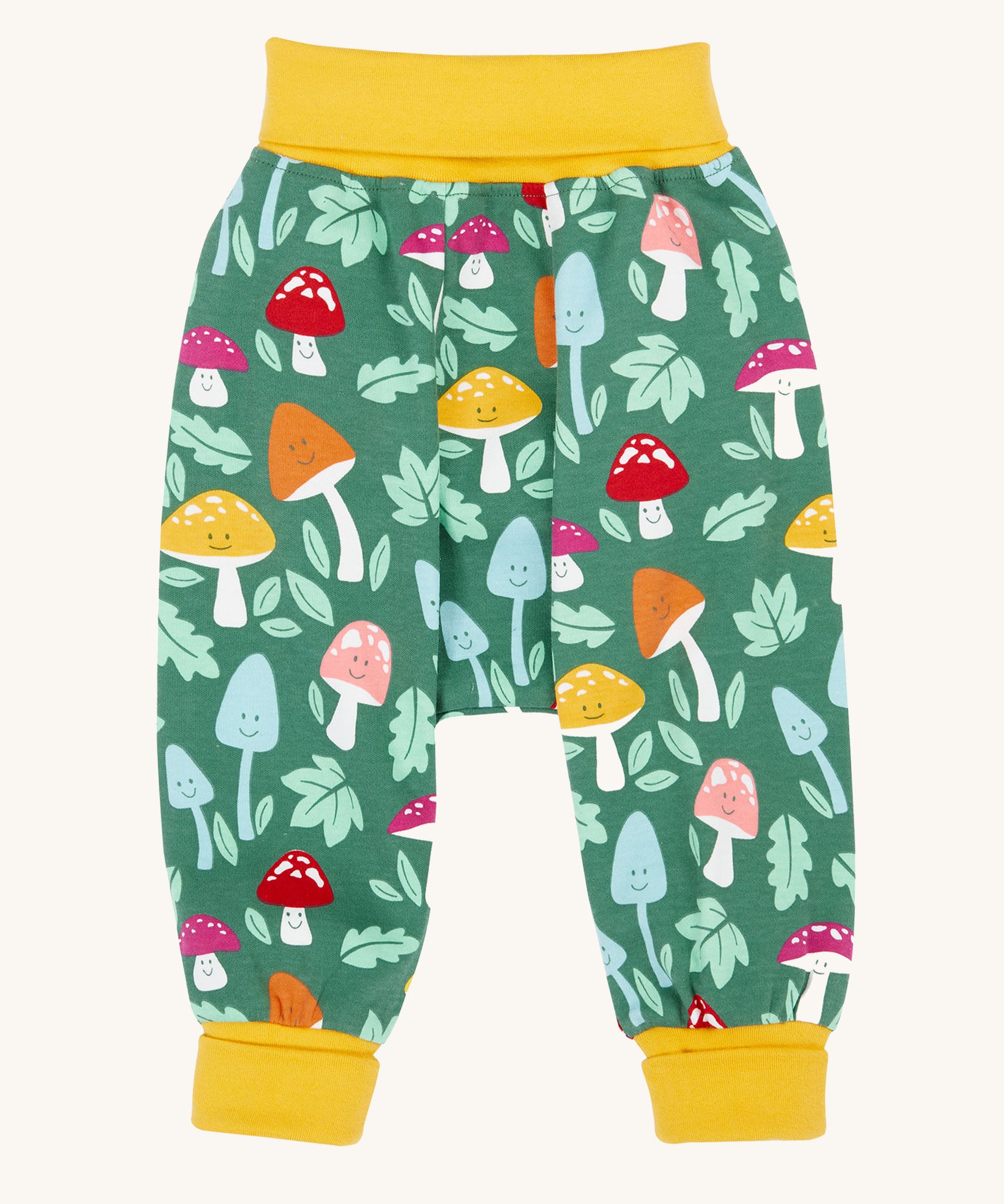 The Frugi fun guys multi coloured mushroom print parsnip pants children's trousers. The print features multi-coloured mushrooms, light green leaves on a dark green background with yellow cold coloured waistband and leg cuffs. 
