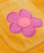 A close up of a pink flower on the Frugi organic cotton Ginny yellow gold Corduroy Pinafore Dress with Flowers with retro flower tights and a rainbow striped top underneath. This dress is a part of a wide range of organic cotton clothing for children available here at Babipur. 