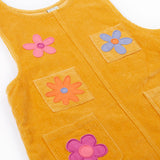 A close up of the Frugi organic cotton Ginny yellow gold Corduroy Pinafore Dress with Flowers with retro  flower tights and a rainbow striped top underneath. This dress is a part of a wide range of organic cotton clothing for children available here at Babipur. 