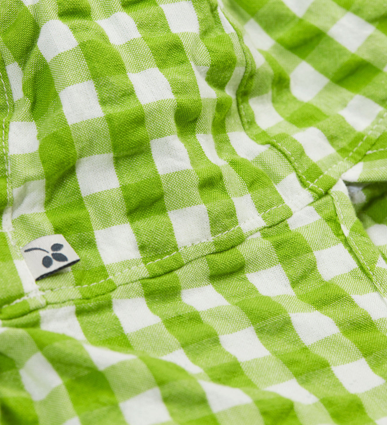 A close up of the Frugi little seersucker sun hat. Showing the stitching between the neck protector and top panel of the hat with the Frugi label on the side on white and green gingham organic cotton fabric