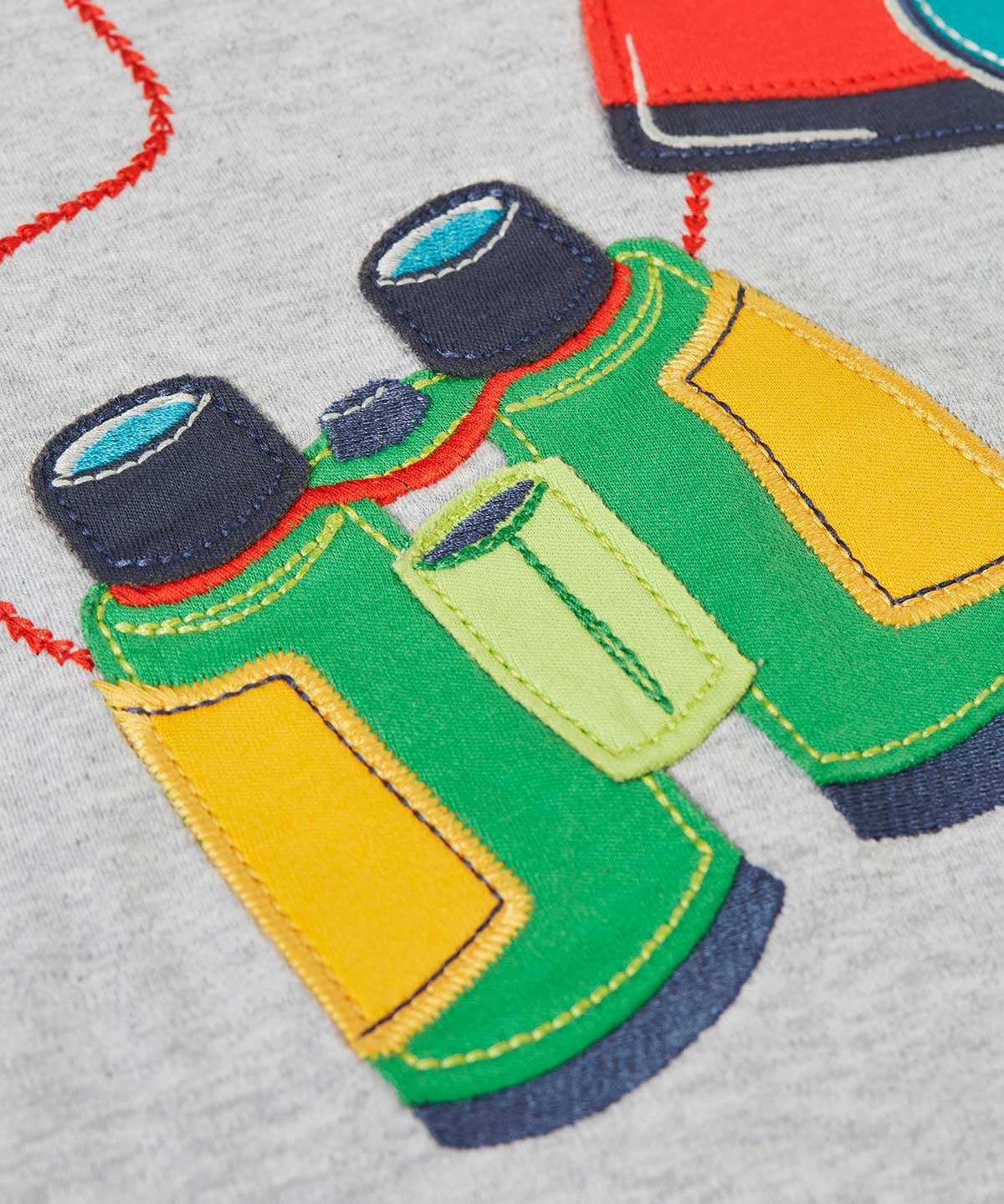 A close up of the green pair of binoculars applique on the front of the  Frugi raglan t-shirt in a grey marl colour with one green and one yellow sleeve and an adventure themed applique design on the front featuring a pair of green binoculars, camera and a wild card compass. 