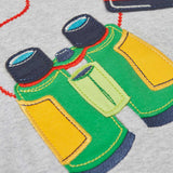 A close up of the green pair of binoculars applique on the front of the  Frugi raglan t-shirt in a grey marl colour with one green and one yellow sleeve and an adventure themed applique design on the front featuring a pair of green binoculars, camera and a wild card compass. 