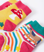 Frugi kids organic cotton grippy socks featuring wild woods designs.  One pair is rainbow striped with a horse and yellow flower grips. The other pair features a mushroom design with green flower grips, one sock is yellow one is pink.