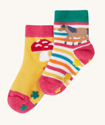 Frugi kids organic cotton grippy socks featuring wild woods designs.  One pair is rainbow striped with a horse and yellow flower grips. The other pair features a mushroom design with green flower grips, one sock is yellow one is pink.