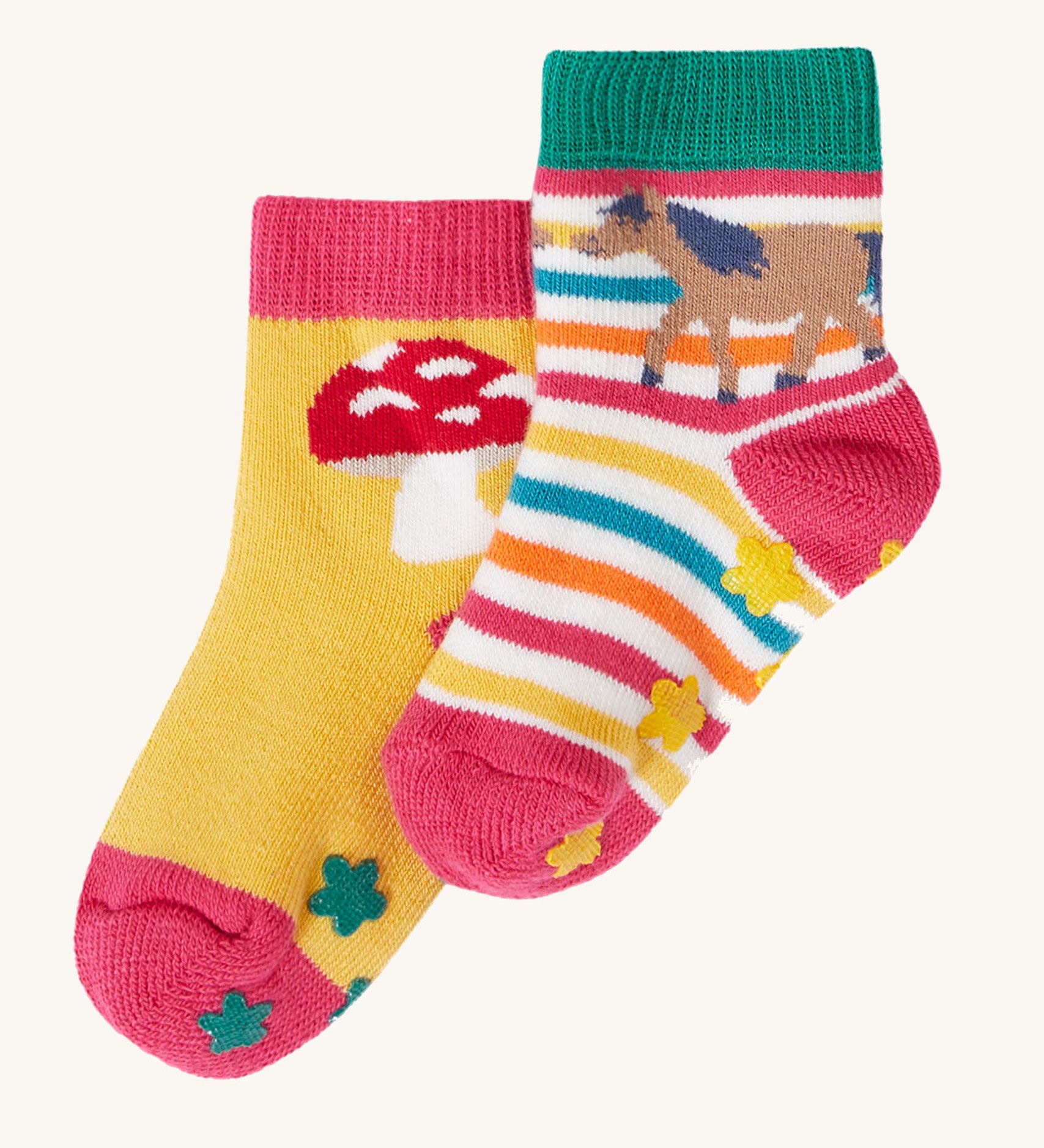 Frugi kids organic cotton grippy socks featuring wild woods designs.  One pair is rainbow striped with a horse and yellow flower grips. The other pair features a mushroom design with green flower grips, one sock is yellow one is pink.